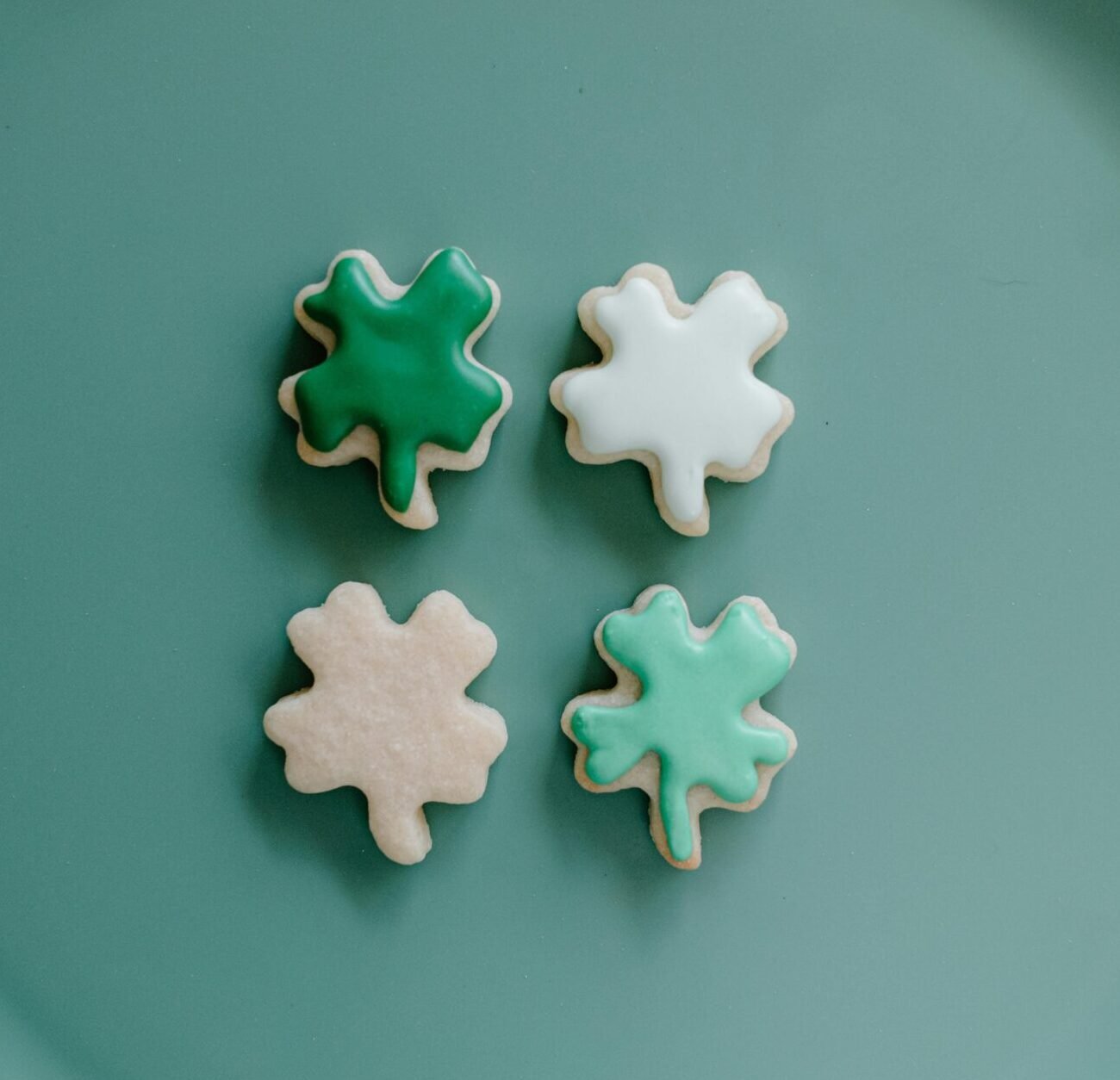 Four charming shamrock-shaped cookies with icing on a teal plate, perfect for St. Patrick's Day celebrations.
